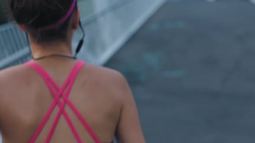 Fit woman running and jogging on a bridge in a city outdoors from the back