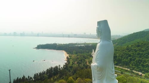 Large White Buddha Statue Standing Tall on Hillside Overlooking Coastal Vietnamese Cityscape with