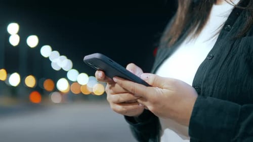 Hände einer Frau mit Handy auf dem Hintergrund der Lichter der Stadt