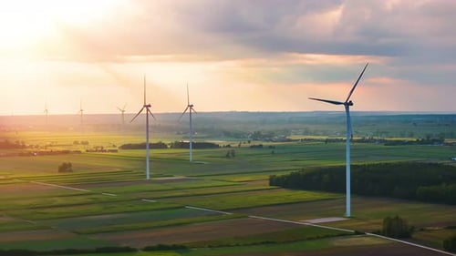Wind turbines generate renewable energy in vast green fields at sunset