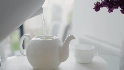 Pouring water into white teapot at home