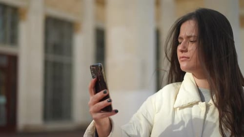Side View Portrait of Worried Young Woman Scrolling Smartphone Touchscreen Standing on City Street