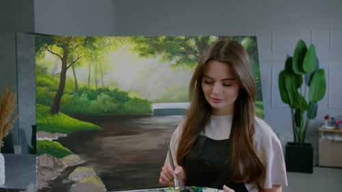 Portrait of a Young Woman is Painting a Picture with a Brush in a Studio