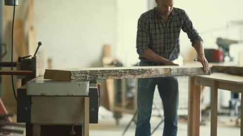 Carpenter Planing a Large Wooden Plank in His Workshop