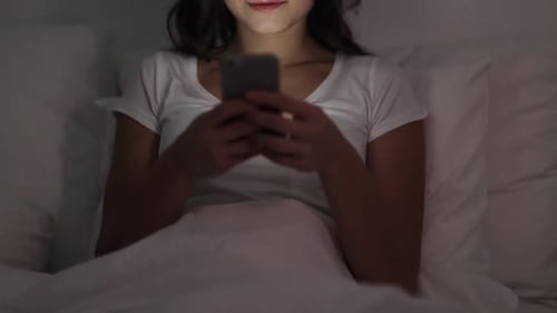 Smiling Young Woman Using Phone in Bed at Night