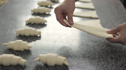 A baker forms a croissant from puff pastry at a bread factory. Close-up of male hands with tattoos.