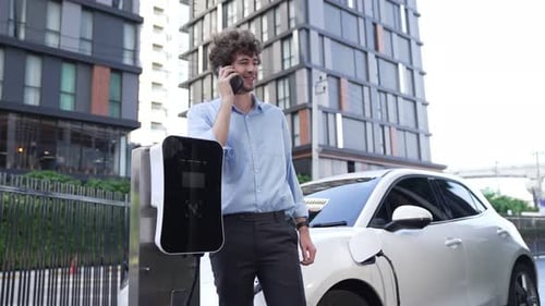 Suitclad Businessman with Progressive Ambition Leaning on His Electric Vehicle