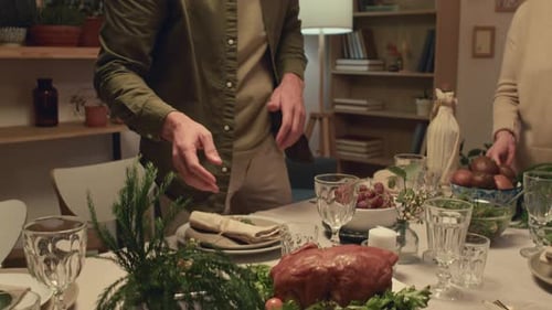 Man Putting Baked Turkey on Table at Thanksgiving with Family