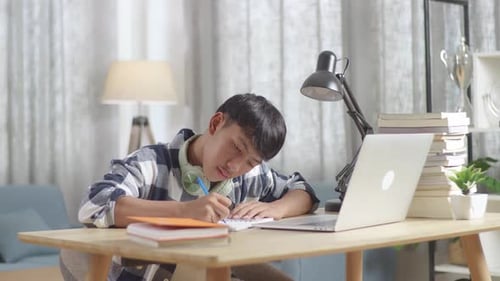 Student Taking Notes at Desk with Laptop