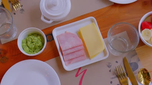 Table top view with breakfast served, it can be seen that there is coffee, fruits, ham, cheese and h