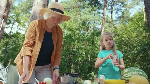 Senior and Girl Preparing Food Outdoors in Nature