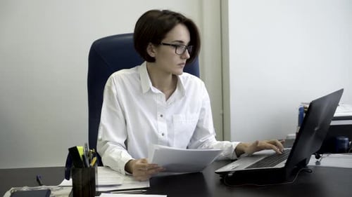Office Worker Checking Documents and Typing on Laptop