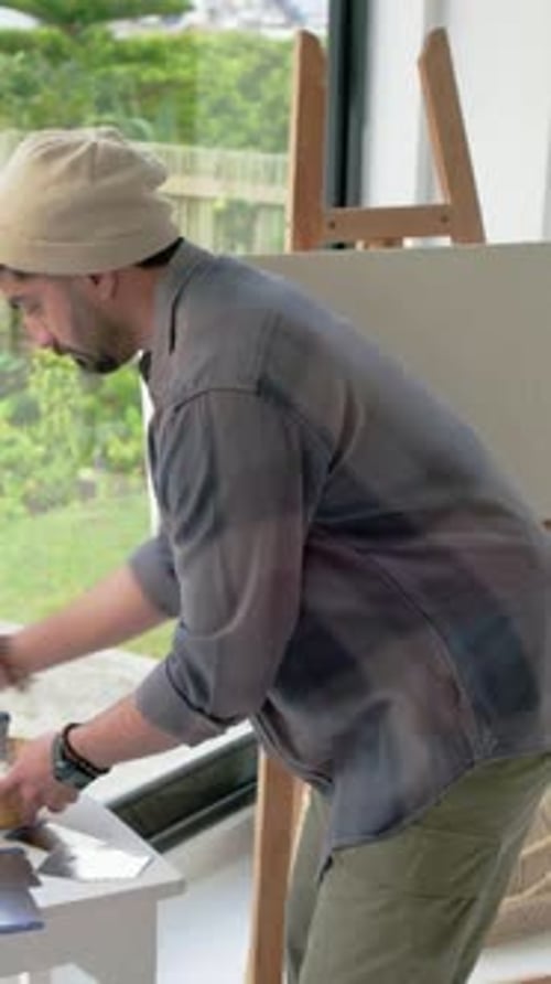 Vidéo verticale : tenant un bol, homme en bonnet et chemise étalant de la pâte sur la table dans un studio d'art