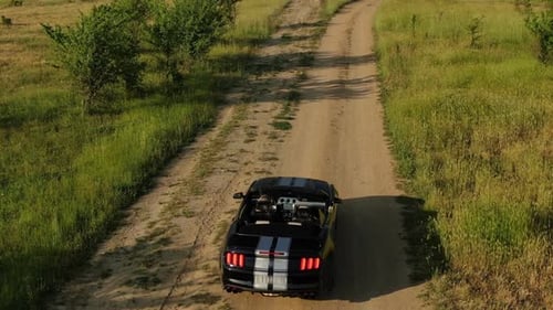 A Black Cabriolet Drives Slowly Along a Dirt Road in the Evening