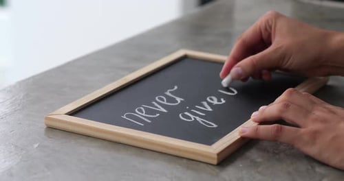 Mains féminines dessinant à la craie sur un tableau noir, phrase de motivation « Ne jamais abandonner »