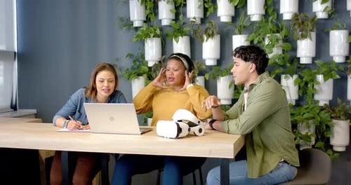 Des collègues diversifiés ouvrent un ordinateur portable, prennent des notes, soulèvent des écouteurs et affinent l'interface VR à table
