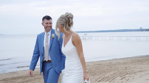 Bride and groom posing elegantly with the ocean waves sparkling behind them