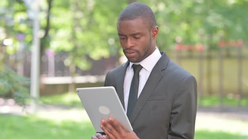 Young Man Uses Tablet Outdoors in Park