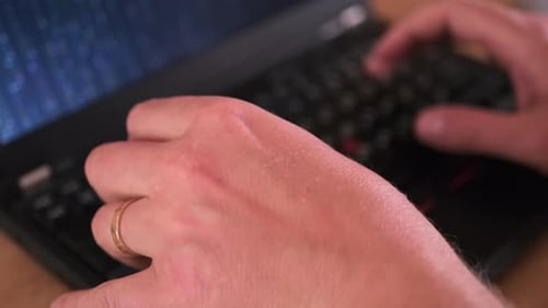Matrix code on laptop screen, close-up male hands, with wedding ring on finger, typing code