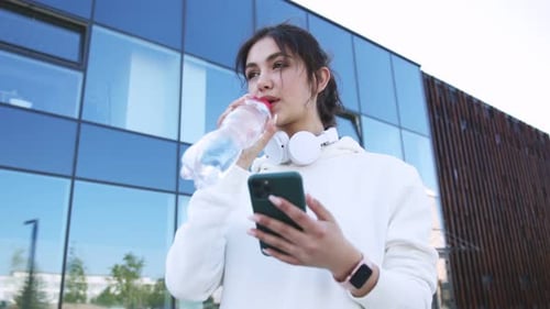Active Woman Hydrates and Uses Phone in City