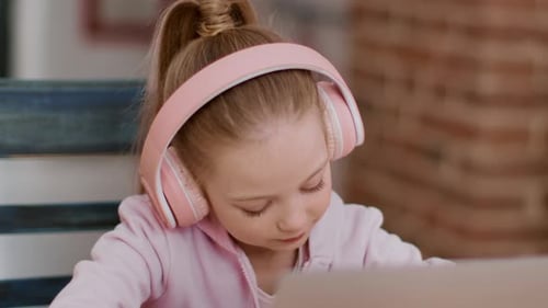 Young Girl Uses Laptop With Headphones Indoors