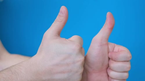 Zwei männliche Hände zeigen Daumen hoch auf hellblauem Hintergrund, sie zeigen Klasse