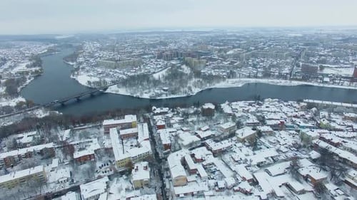 Río retorcido que divide la gran ciudad en dos partes. Panorama urbano en el frío, sombrío y nevado día de invierno