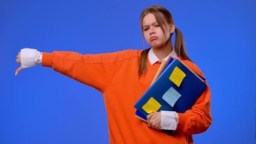 A Young Female Student Gives a Thumbs Down Gesture While Holding Folders and Notes in Her Hands