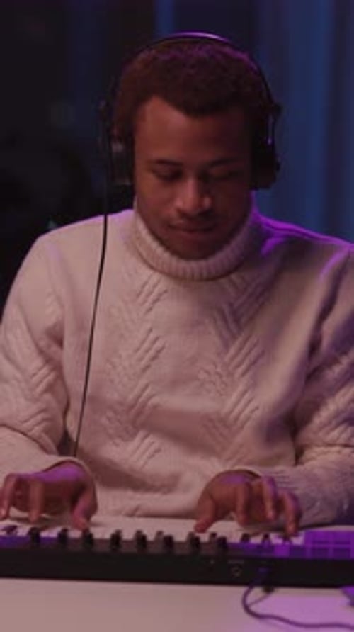 Man Plays Keyboard with Headphones in Dimly Lit Room