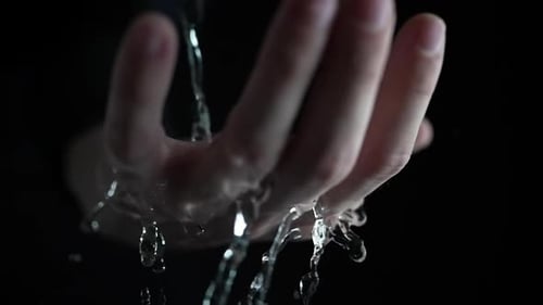 Mano con gotas de agua cayendo sobre fondo oscuro