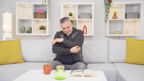 Man Rubbing Elbow in Pain on Couch