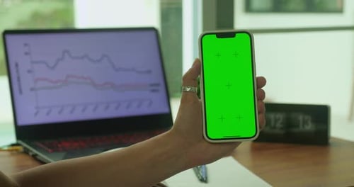 A Woman's Hand Phone with Green Mockup Screen Chroma Key Holds a Smartphone of the Workspace