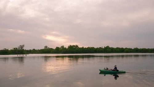 Lone kayaker paddling across serene lake at sunset