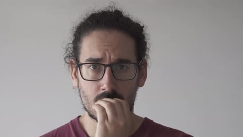Close up of anxious young man biting his nails and looking at the camera