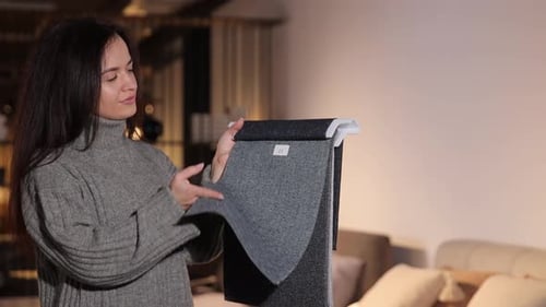 A Pretty Woman with Dark Hair Chooses Upholstery for Her Sofa in a Furniture Store