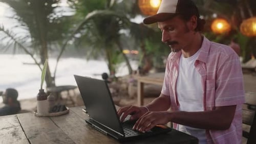 Mann programmiert auf Laptop im Strandcafé bei Sonnenuntergang Freiberuflicher Programmierer arbeitet von Sea Männlicher Entwickler