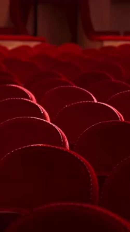 Selective focus on empty rows with red velvet seats in theater hall. Rows with empty chairs.