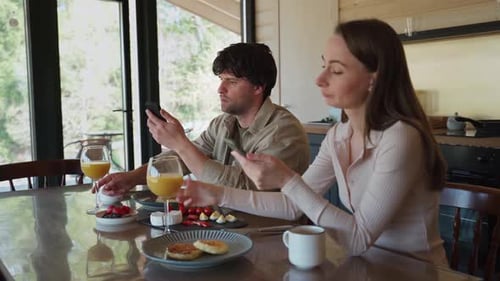 Couple Consumed by Phones During Breakfast Inside