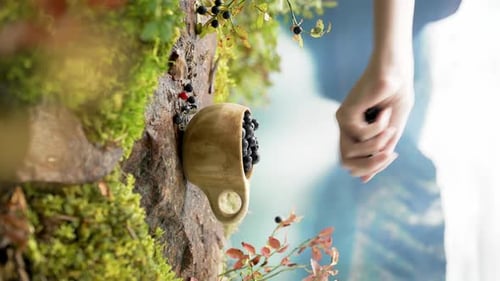 Hand Adding Blueberries to Wooden Mug Outdoors