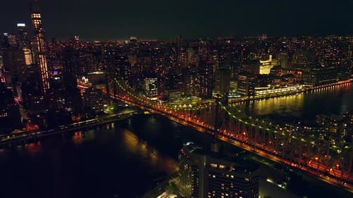 Beautiful Queensboro Bridge in lights at night time. Hundreds of cars moving by the bridge and roads