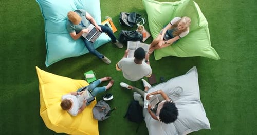 Above view of creative students collaborating on a project, sitting on bean bags in an office setup