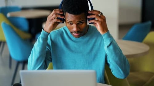 Young Adult Working With Laptop Puts On Headphones