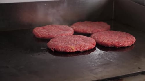 Closeup of Four Burger Patties Fried on a Hot Stove in the Restaurant Kitchen