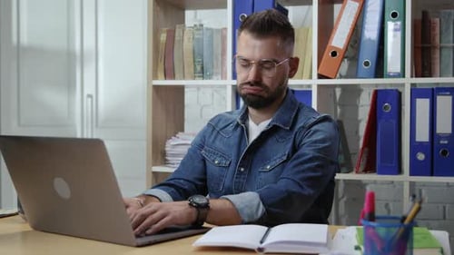 Jovem desmotivado sentado à mesa com laptop sentindo estresse e desinteresse pelo trabalho, entediante