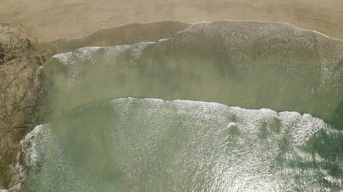 Aerial view of gentle surf washing over shallow sandy coast in sunlight