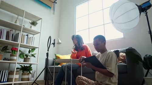 Joven influencer de belleza asiática haciendo un vídeo tutorial de maquillaje ayudada por su asistente en casa