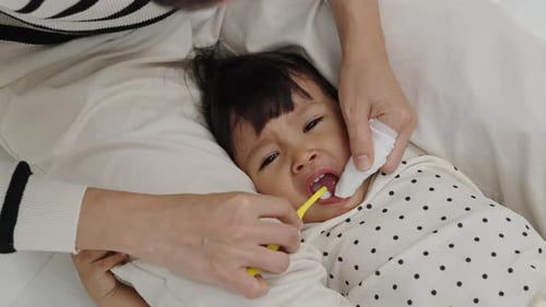 Mother brushes little girl's teeth in bed