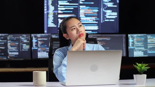 Programmeuse pensant à quelque chose tout en écrivant du code sur un ordinateur portable à l'aide de plusieurs moniteurs