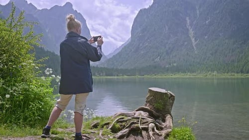 Woman tourists takes phone photo of scenic lake with mountain backdrop
