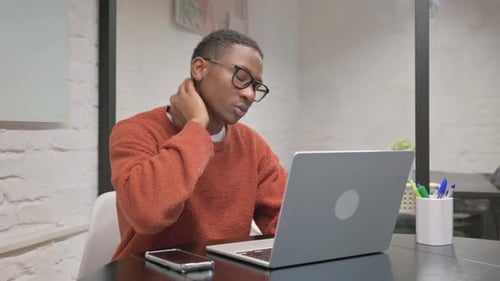 Young Adult Massaging Neck While Working on Laptop
